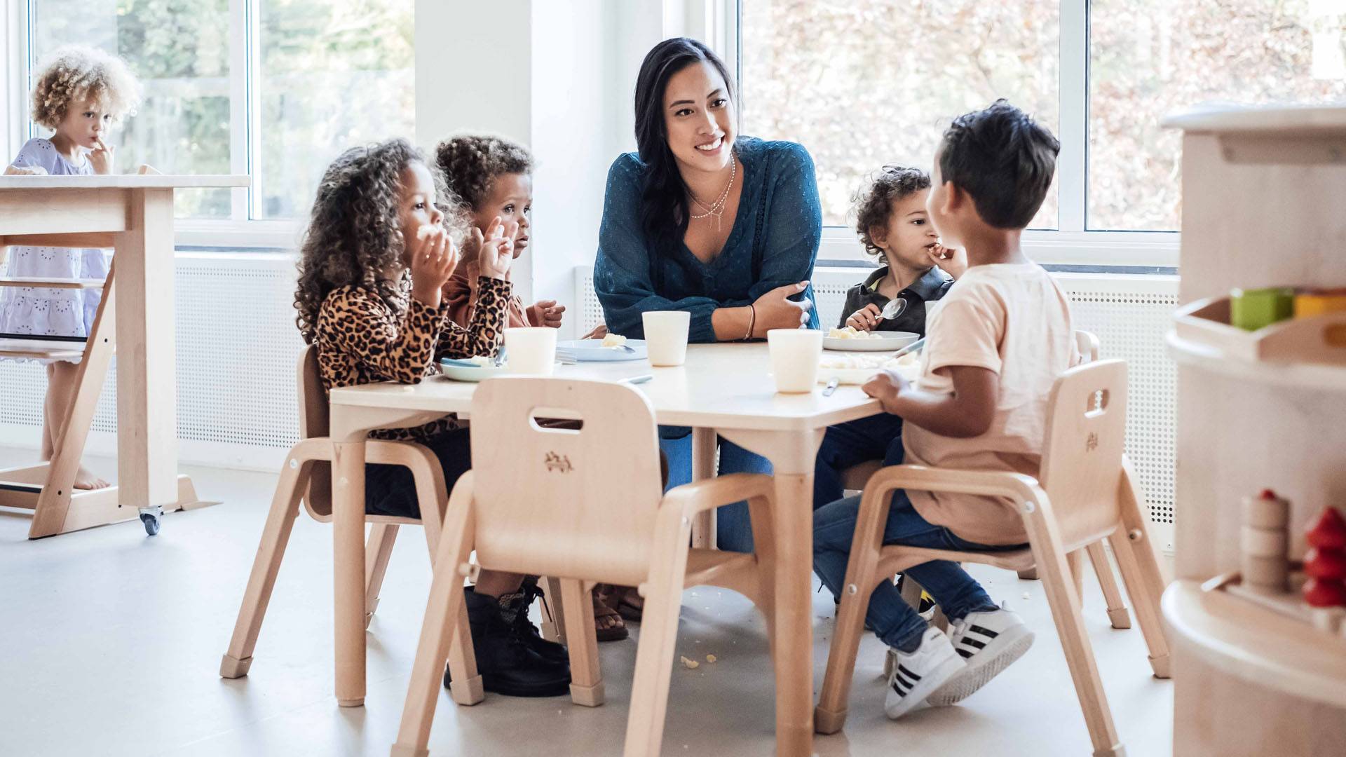 Pedagogisch medewerker eet aan tafel samen met peuters bij Kindergarden kinderopvang